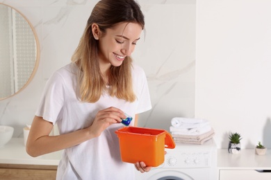 Photo of Woman holding container with laundry detergent capsules in bathroom