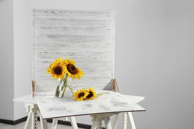 Photo of Glass vase with beautiful sunflowers and double-sided backdrop on table in photo studio