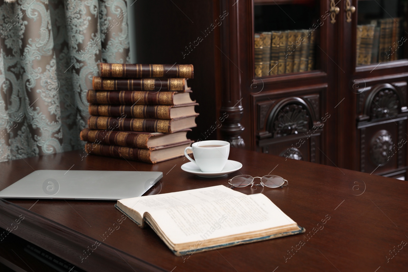 Photo of Laptop, books and cup of coffee on wooden table in library reading room