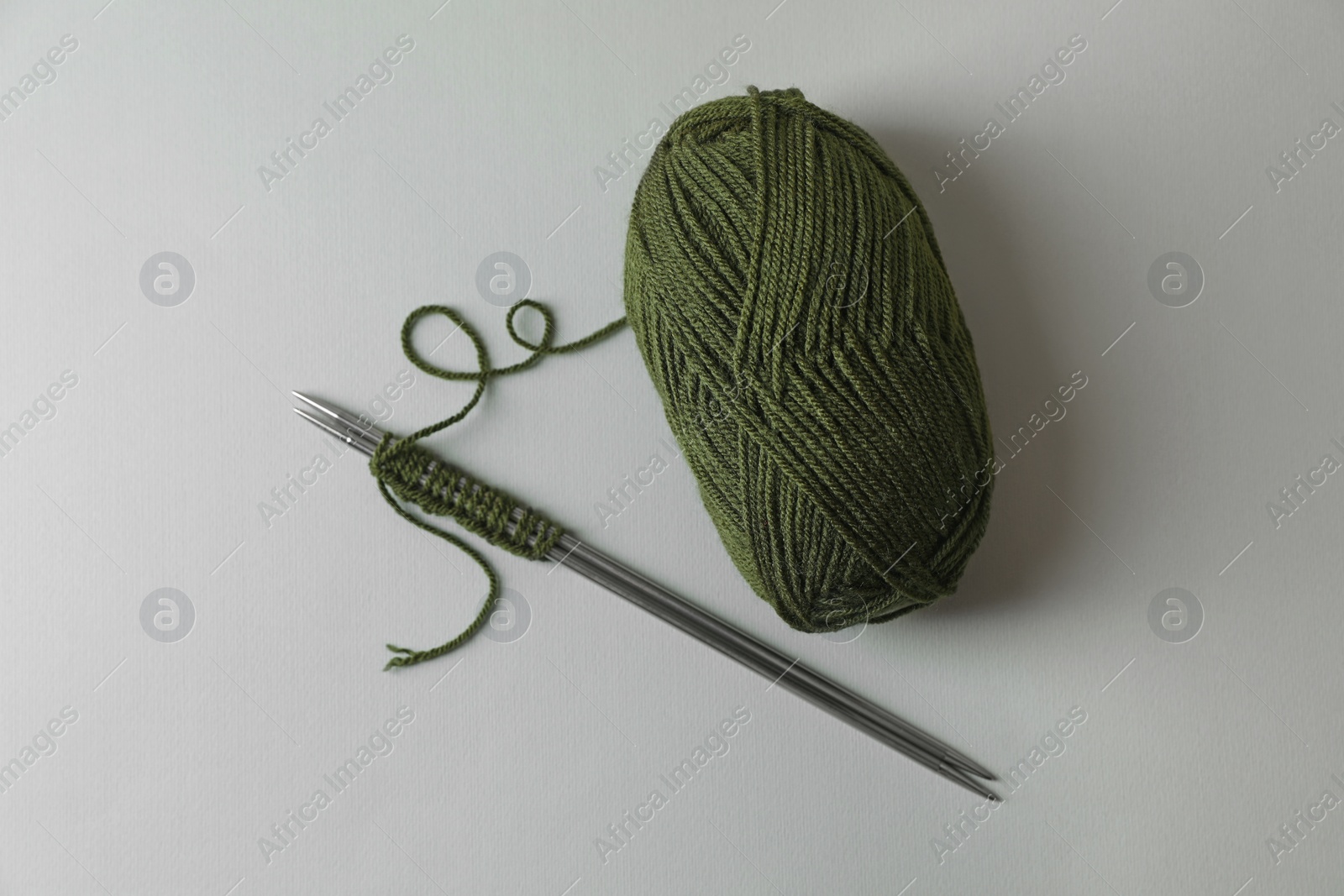 Photo of Soft green yarn, knitting and metal needles on light background, top view