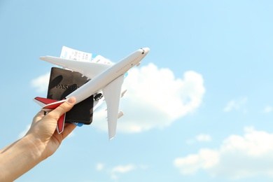Photo of Woman holding toy airplane and passport with tickets against blue sky, closeup