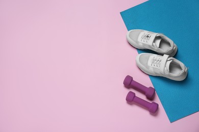 Photo of Exercise mat, dumbbells and shoes on pink background, flat lay. Space for text