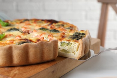 Photo of Taking piece of delicious homemade quiche with salmon and broccoli from wooden board on white table, closeup