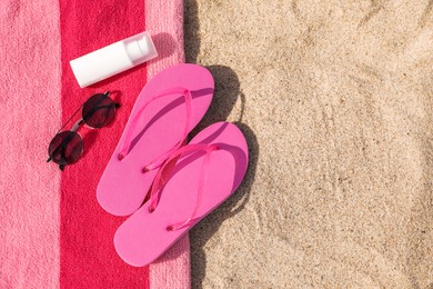 Photo of Beach towel with slippers, sunglasses and sunscreen on sand, top view. Space for text