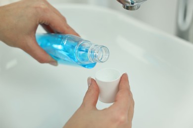 Photo of Young woman using mouthwash above sink in bathroom, closeup