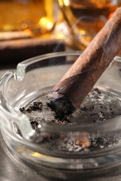 Ashtray with smoldering cigar on grey table, closeup