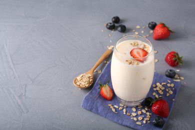 Tasty yogurt in glass, oats and berries on grey table, space for text