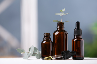 Photo of Bottles of essential oil and eucalyptus on white table. Space for text