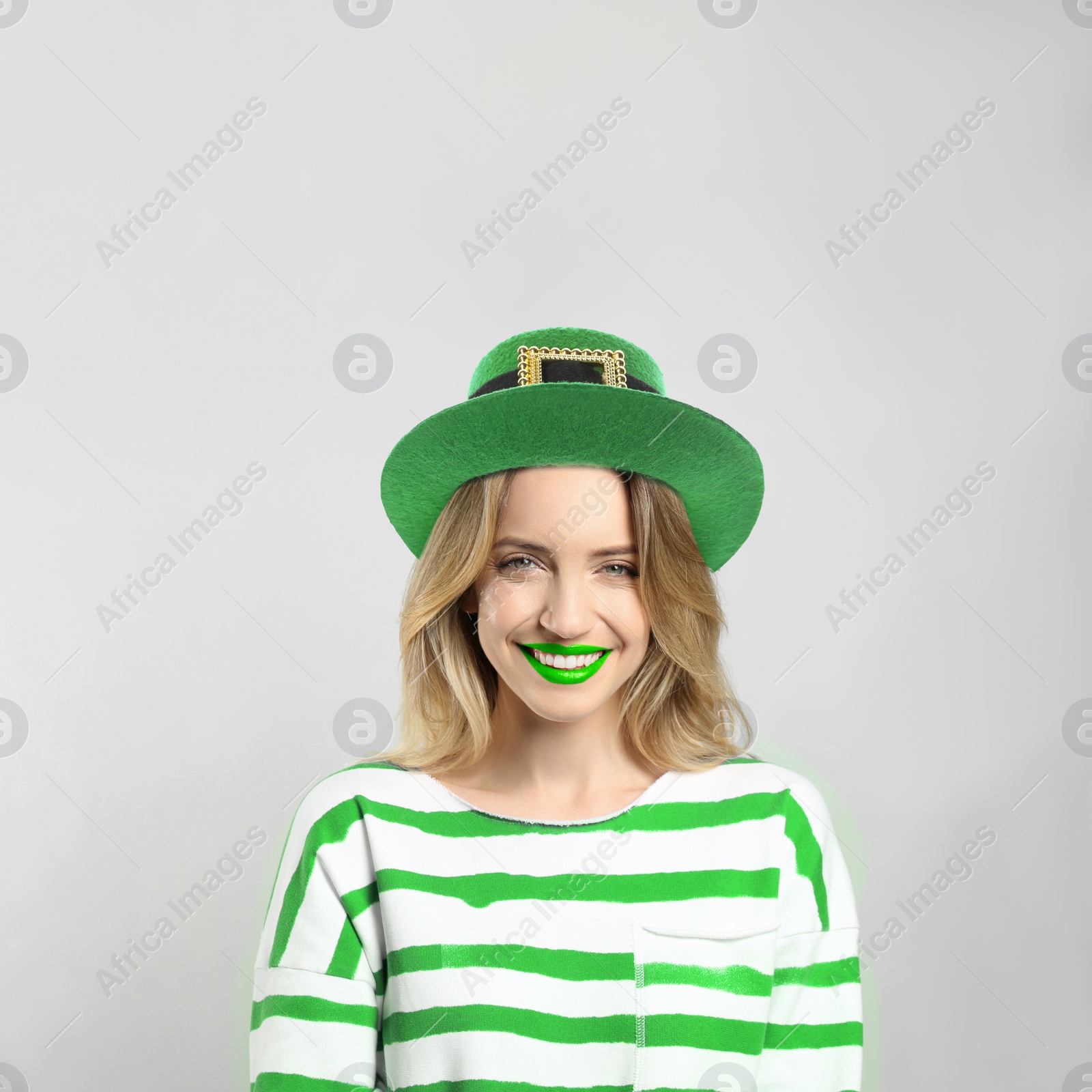 Image of St. Patrick's day party. Pretty woman with green lips in leprechaun hat on light grey background