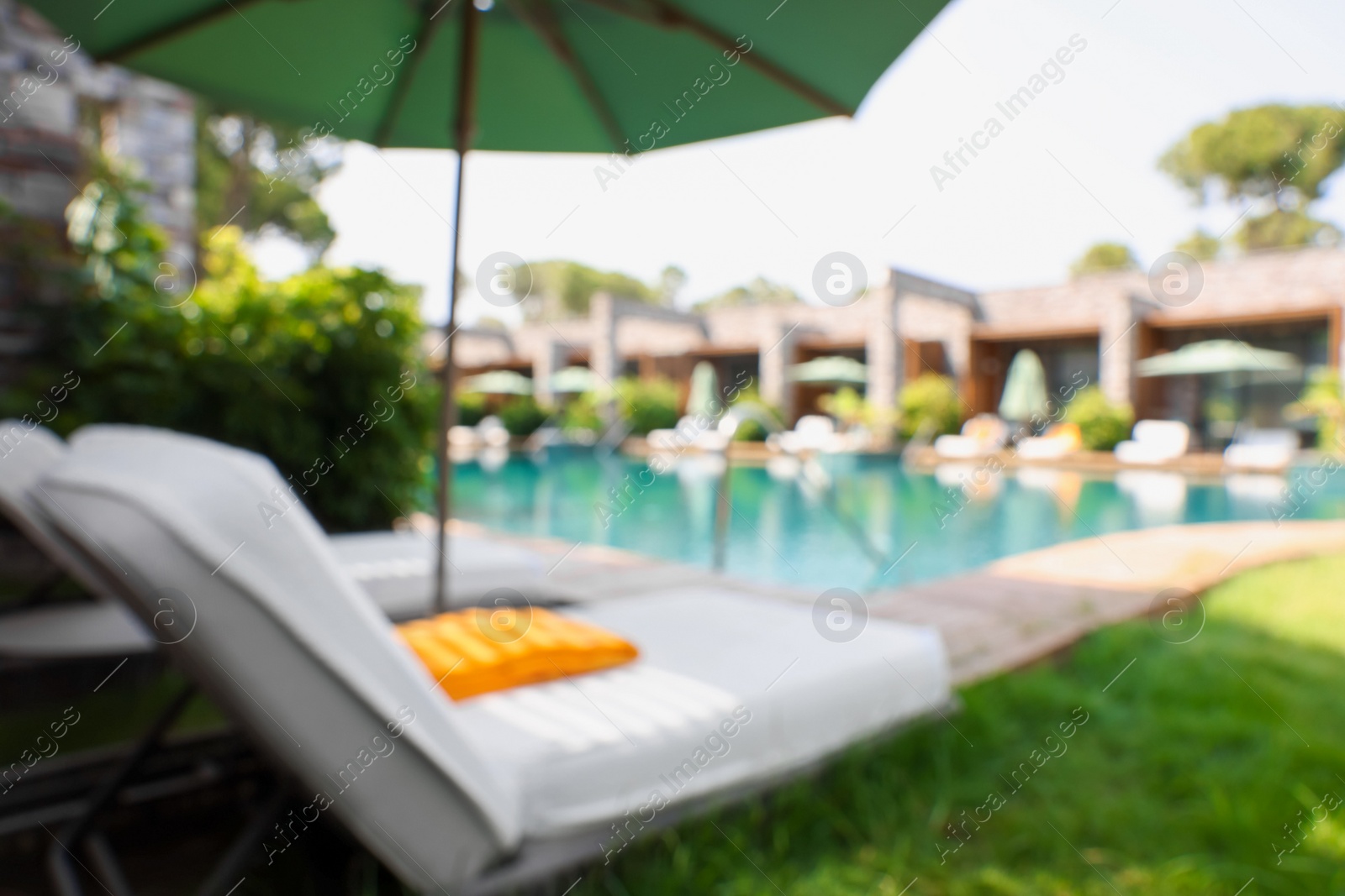 Photo of Sunbeds near swimming pool at luxury resort, blurred view