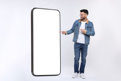 Man pointing at huge mobile phone with empty screen on grey background. Mockup for design