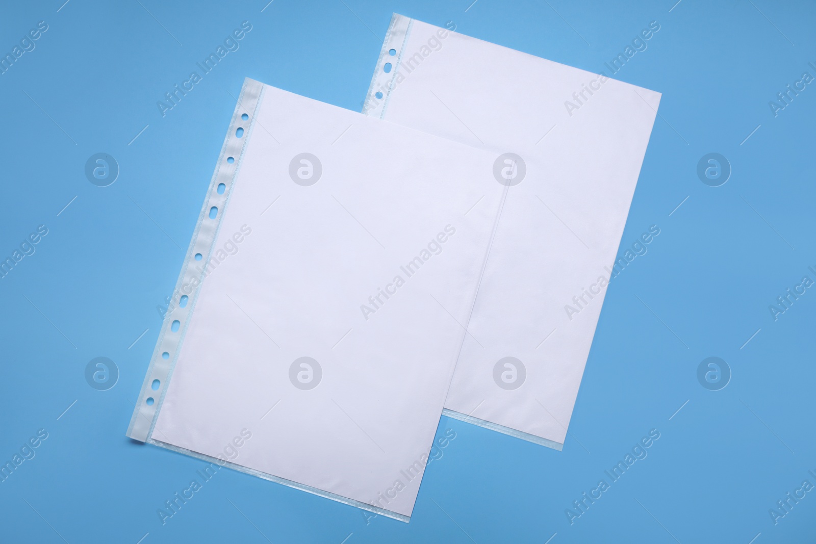 Photo of Punched pockets with paper sheets on light blue background, flat lay. Space for text