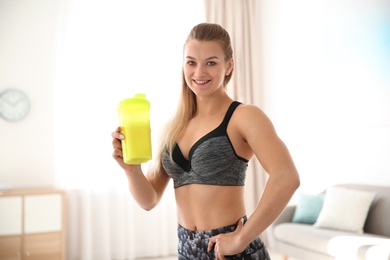 Photo of Young sporty woman with bottle of protein shake at home