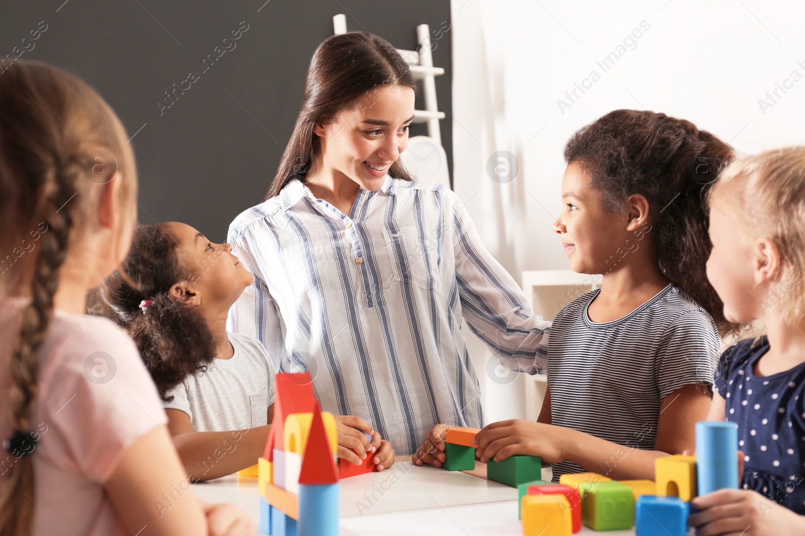 Photo of Cute little children and nursery teacher playing with building blocks in kindergarten. Indoor activity