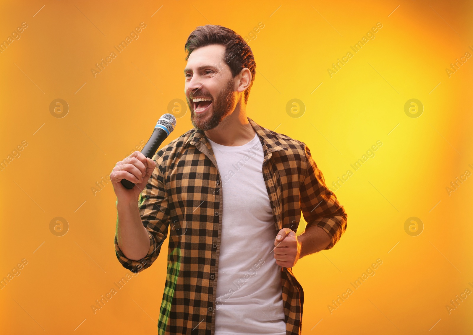 Photo of Handsome man with microphone singing on golden background