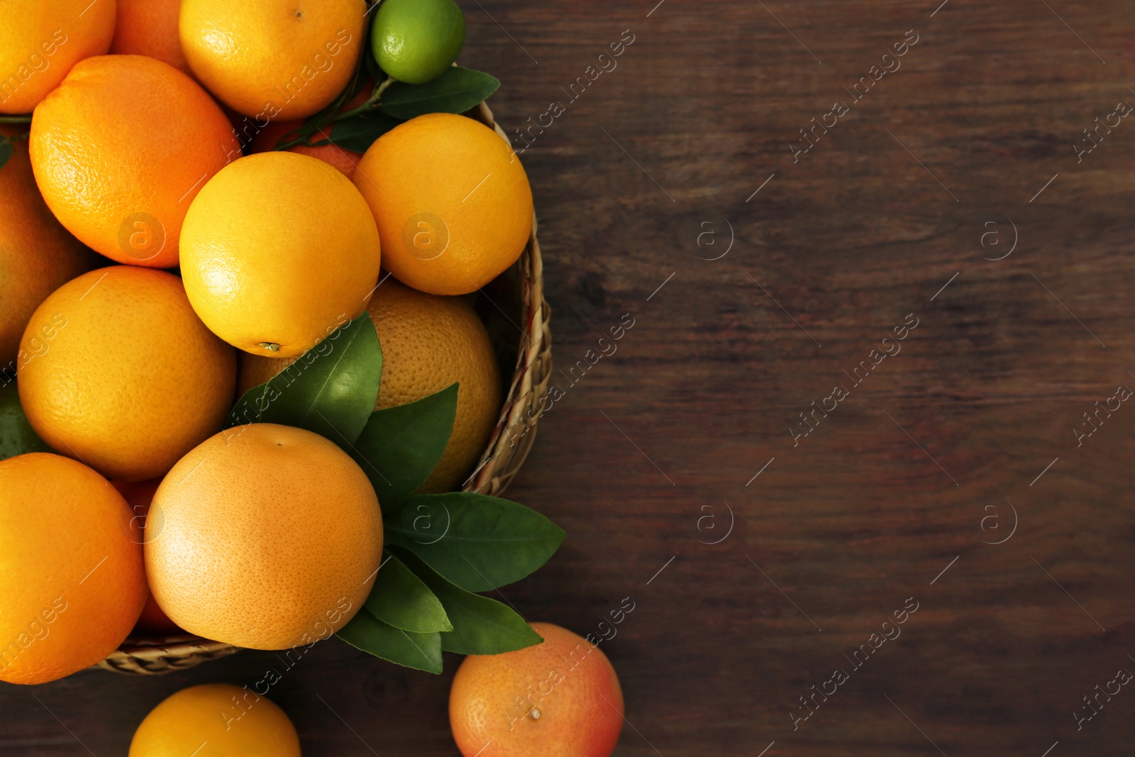 Photo of Wicker basket with different citrus fruits and leaves on wooden table, top view. Space for text