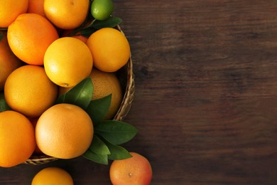 Photo of Wicker basket with different citrus fruits and leaves on wooden table, top view. Space for text