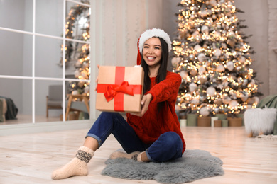 Happy young woman in Santa hat with Christmas gift at home