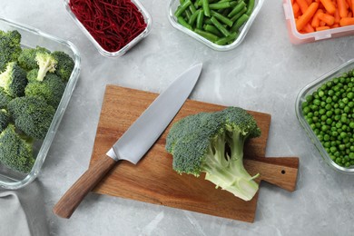 Photo of Wooden board with broccoli, knife and containers with fresh products on light gray marble table, flat lay. Food storage