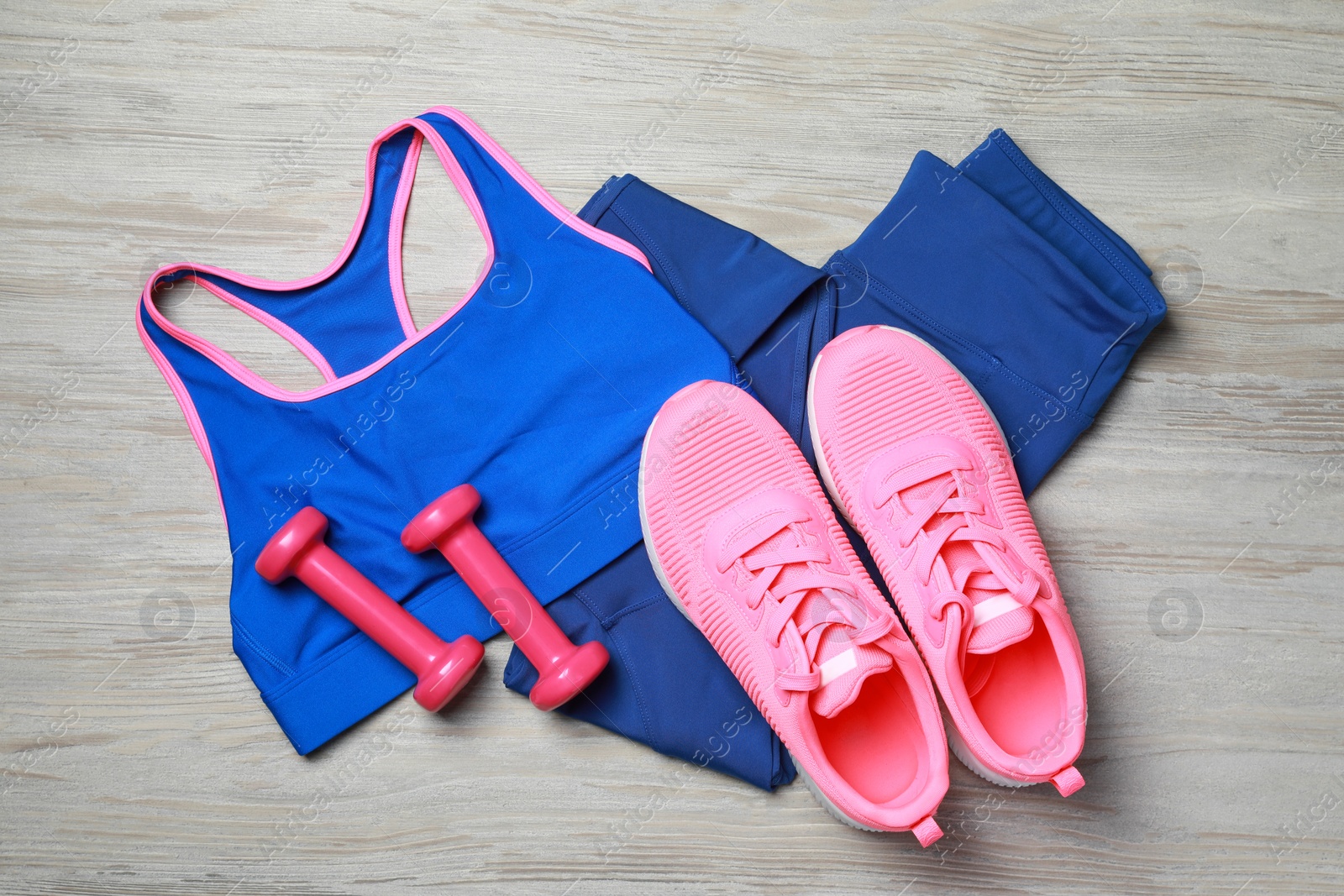 Photo of Stylish sportswear and dumbbells on wooden background, flat lay