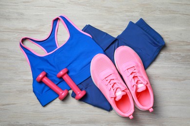 Stylish sportswear and dumbbells on wooden background, flat lay