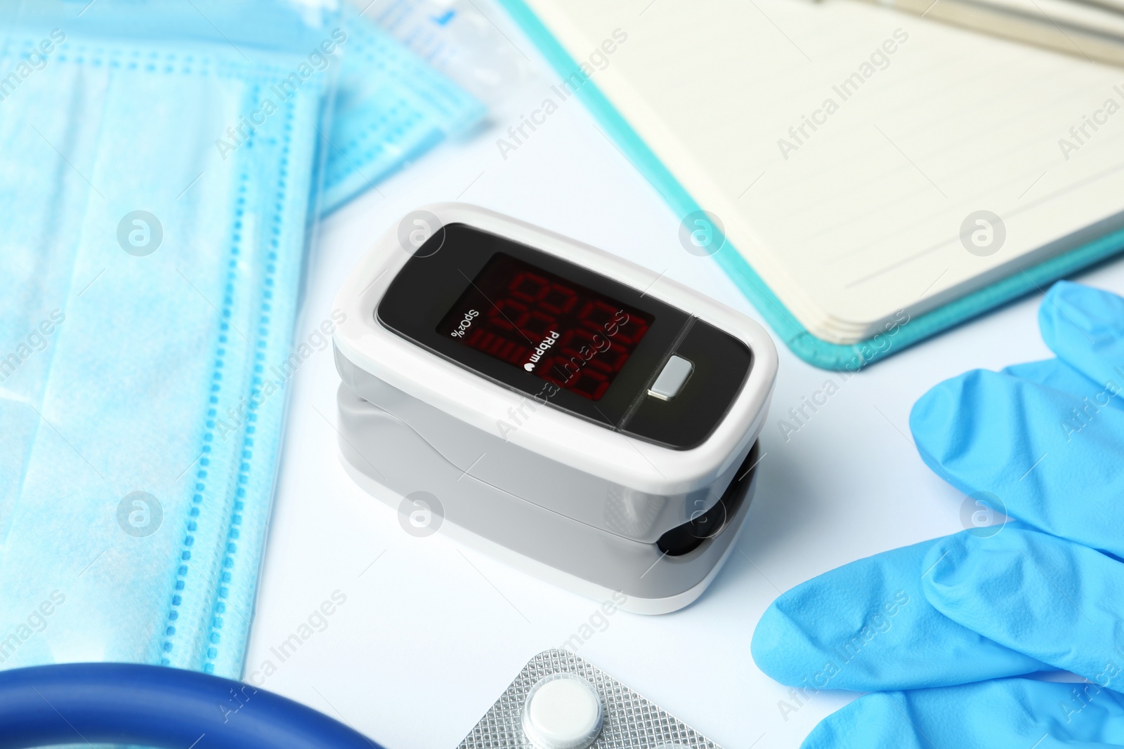 Photo of Modern fingertip pulse oximeter and medical items on white background, closeup