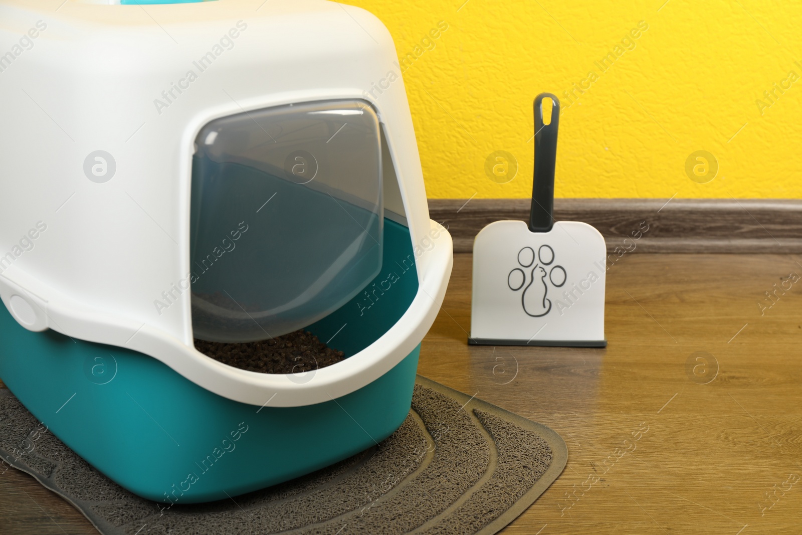 Photo of Cat litter box and scoop on floor near yellow wall