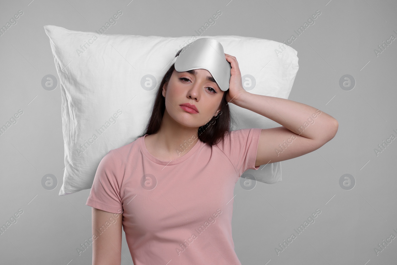 Photo of Tired young woman with sleep mask and pillow on light grey background. Insomnia problem