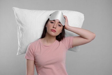 Tired young woman with sleep mask and pillow on light grey background. Insomnia problem
