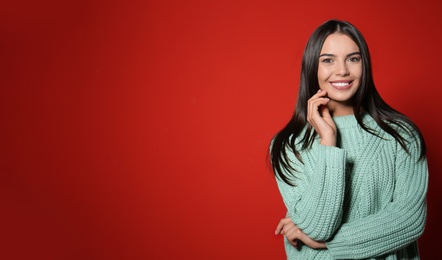 Young woman in warm sweater on red background. Space for text