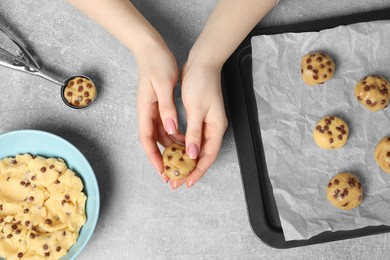 Woman making delicious chocolate chip cookies at light grey table, top view