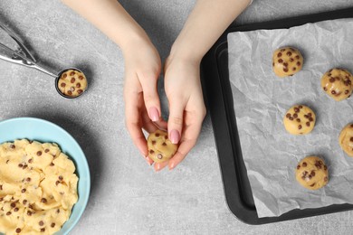 Photo of Woman making delicious chocolate chip cookies at light grey table, top view