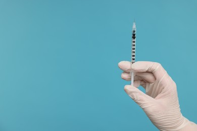 Photo of Doctor holding syringe on light blue background, closeup. Space for text