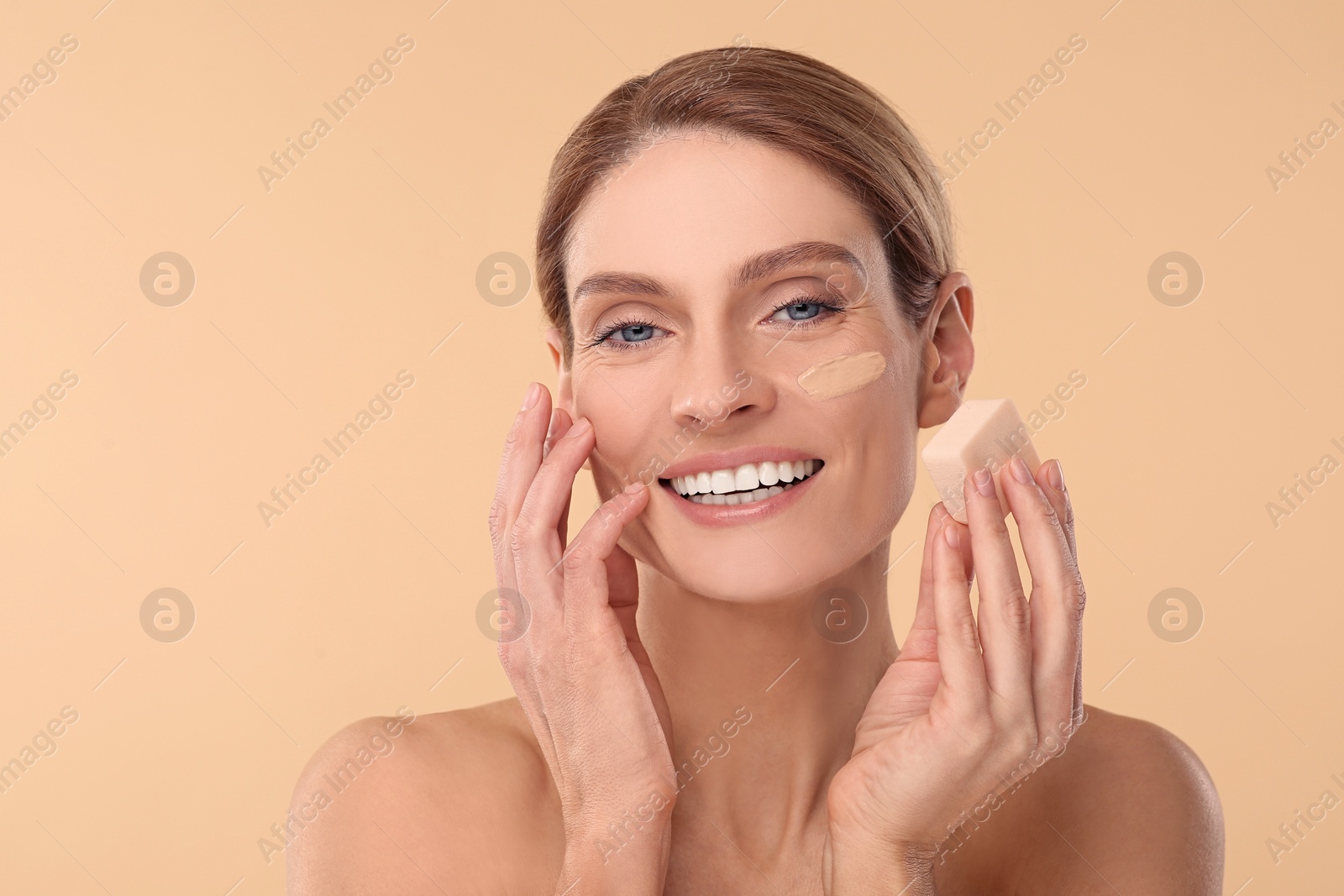 Photo of Woman blending foundation on face with makeup sponge against beige background