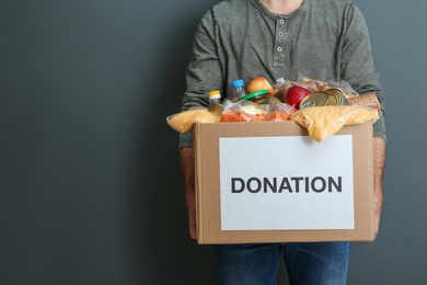 Photo of Man holding donation box with food on gray background, closeup. Space for text