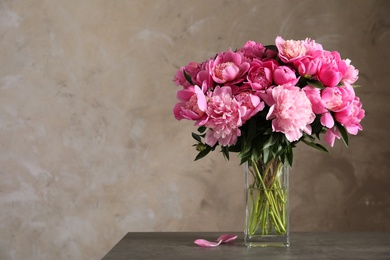 Photo of Fragrant peonies in vase on table against color background, space for text. Beautiful spring flowers