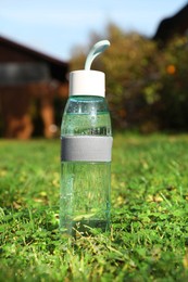 Glass bottle of fresh water on green grass outdoors