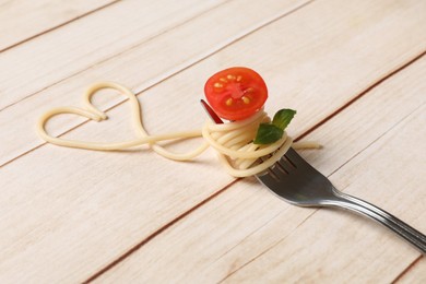 Photo of Heart made of tasty spaghetti, fork, tomato and basil on wooden table, closeup