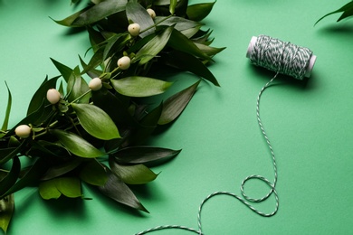 Photo of Beautiful handmade mistletoe wreath and thread spool on green background, closeup. Traditional Christmas decor