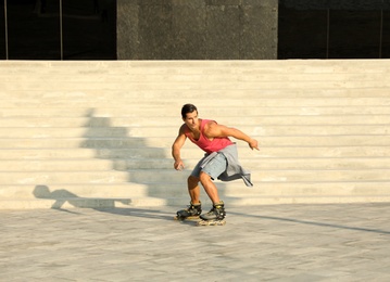 Photo of Handsome young man roller skating on city street, space for text