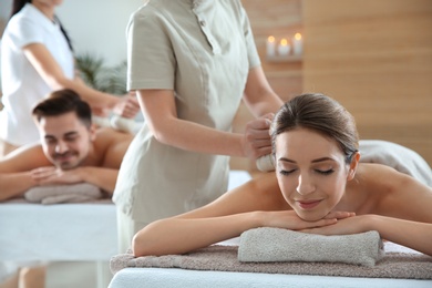 Romantic young couple enjoying herbal bag massage in spa salon