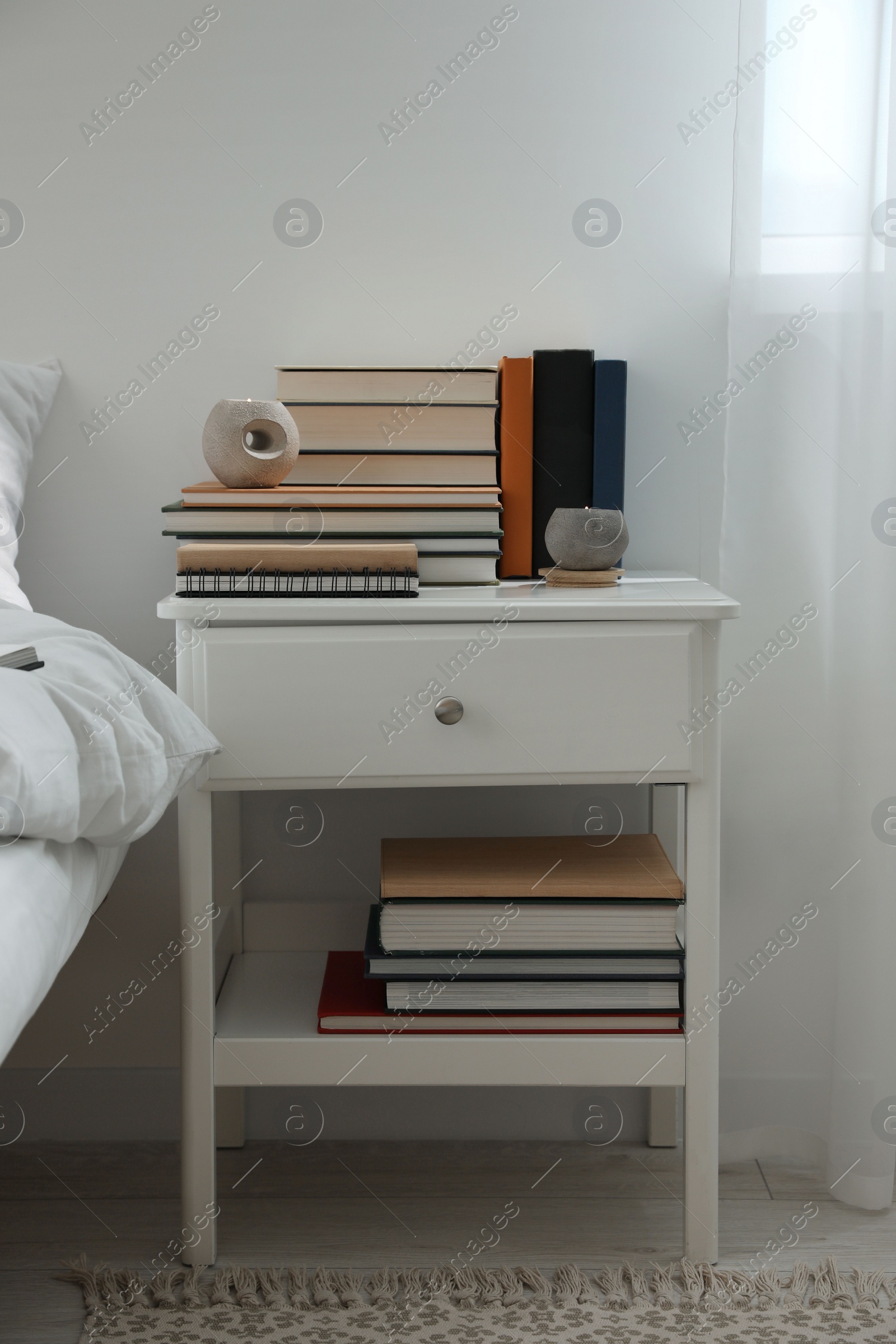 Photo of Hardcover books and scented candles on white bedside table indoors