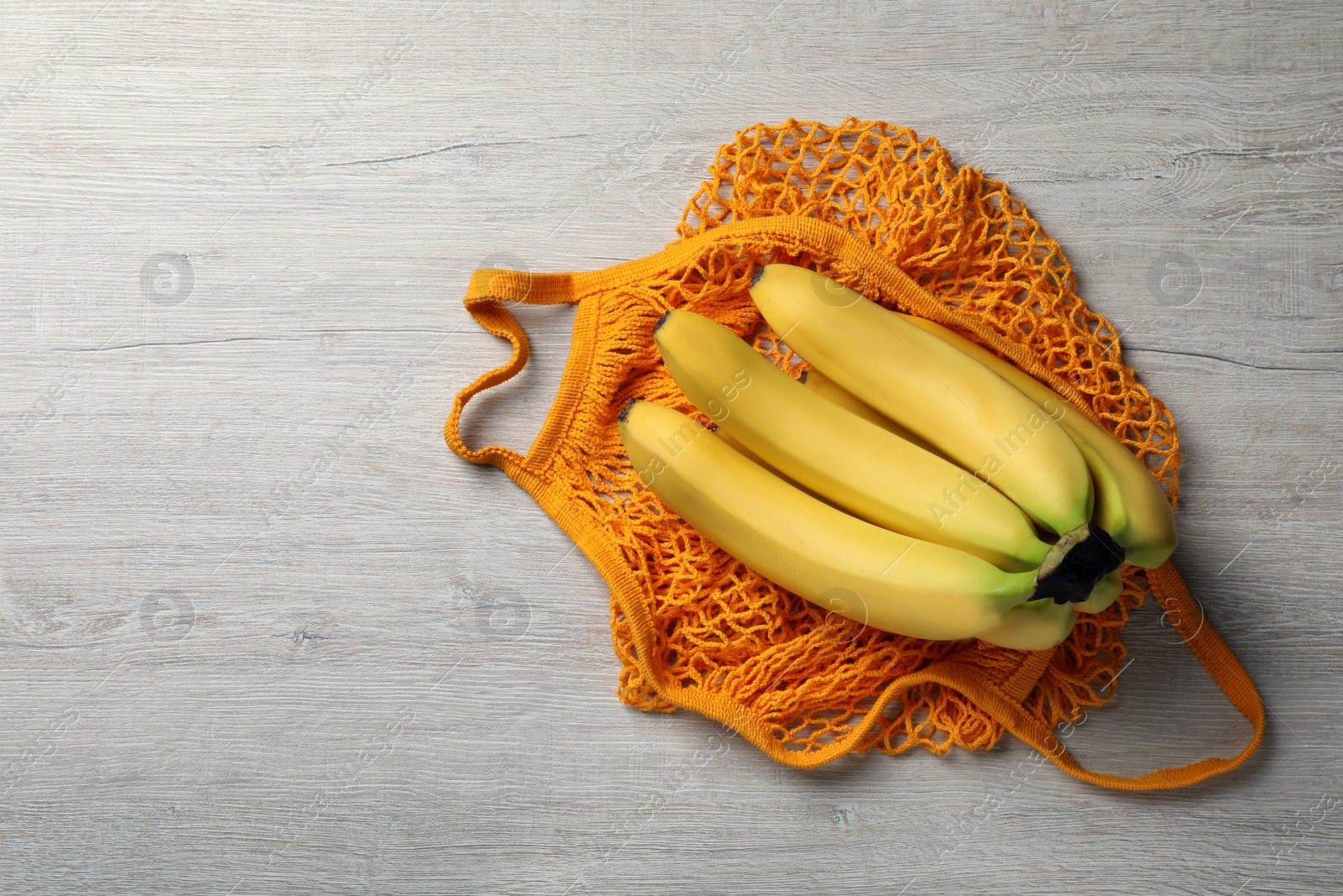 Photo of Net bag with bananas on white wooden table, top view. Space for text