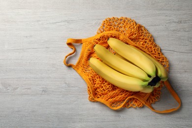 Photo of Net bag with bananas on white wooden table, top view. Space for text