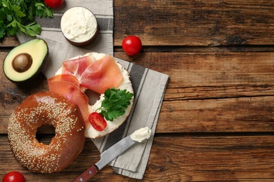 Photo of Delicious bagel with cream cheese, jamon, tomato and parsley on wooden table, flat lay. Space for text