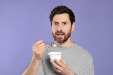 Photo of Handsome man eating delicious yogurt on violet background