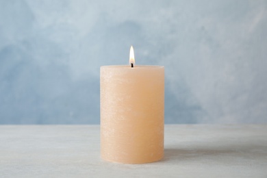 Photo of Burning candle on table against color background