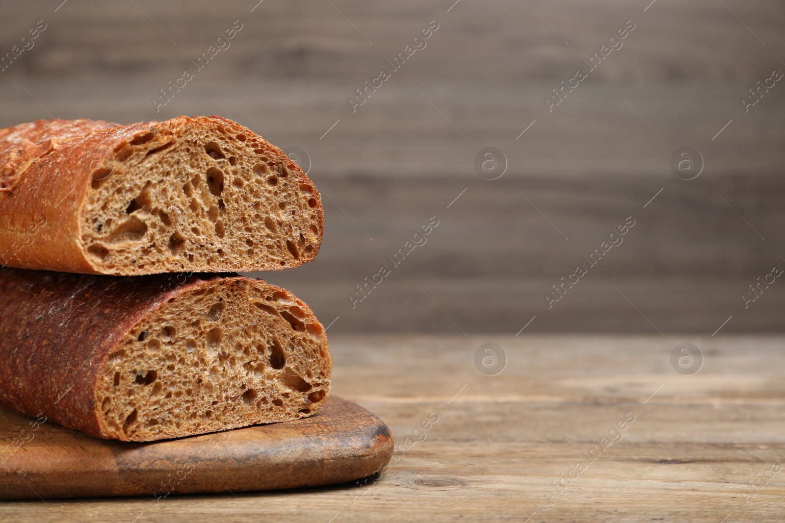 Photo of Cut rye baguette on wooden table, closeup. Space for text