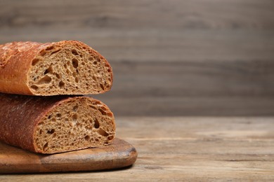 Photo of Cut rye baguette on wooden table, closeup. Space for text