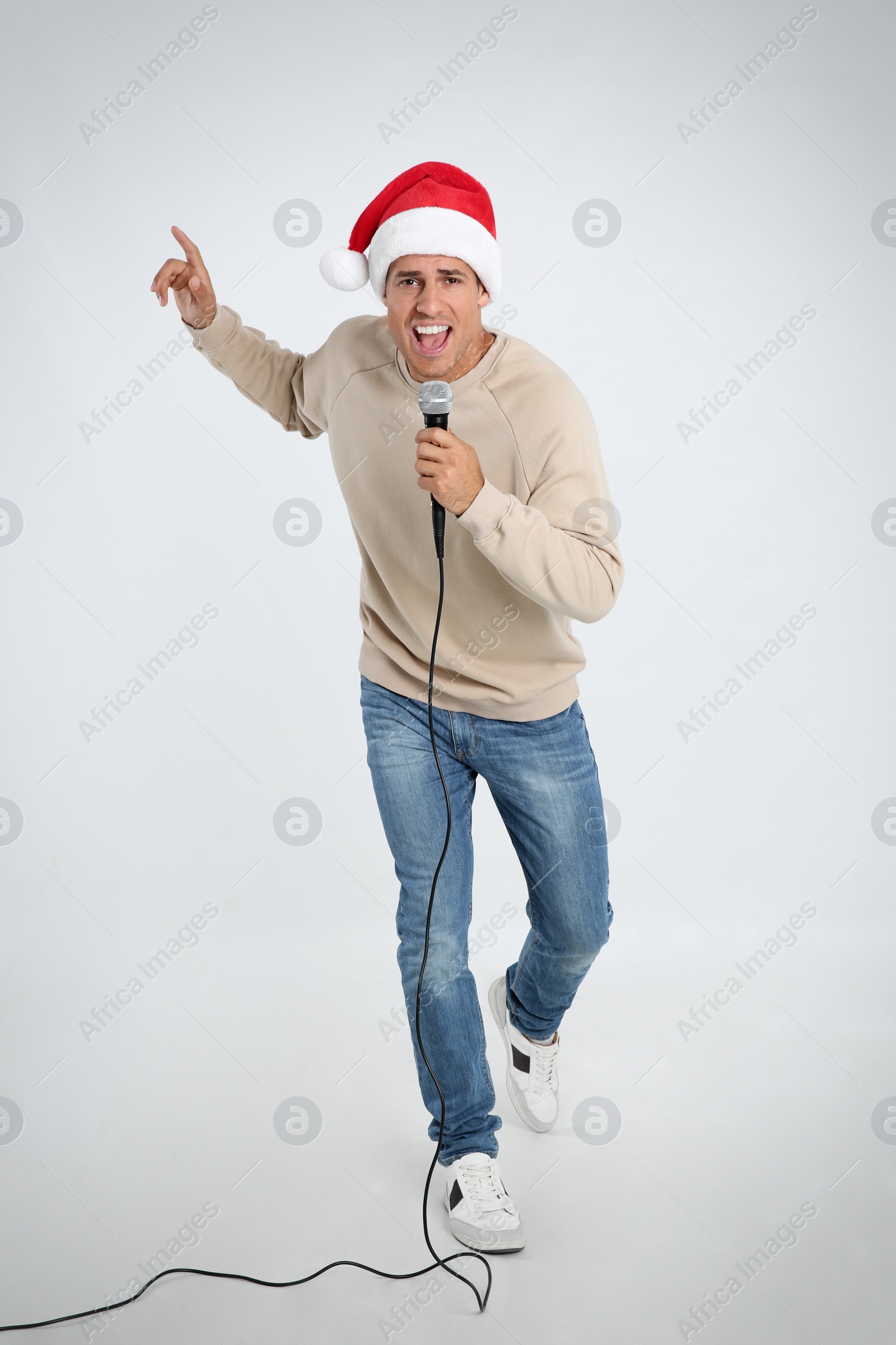 Photo of Emotional man in Santa Claus hat singing with microphone on white background. Christmas music